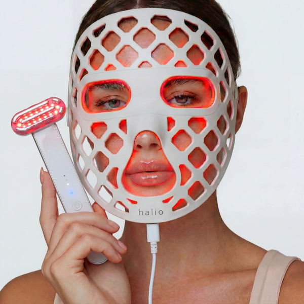Person wearing a LED face mask with a handheld device, on a plain background