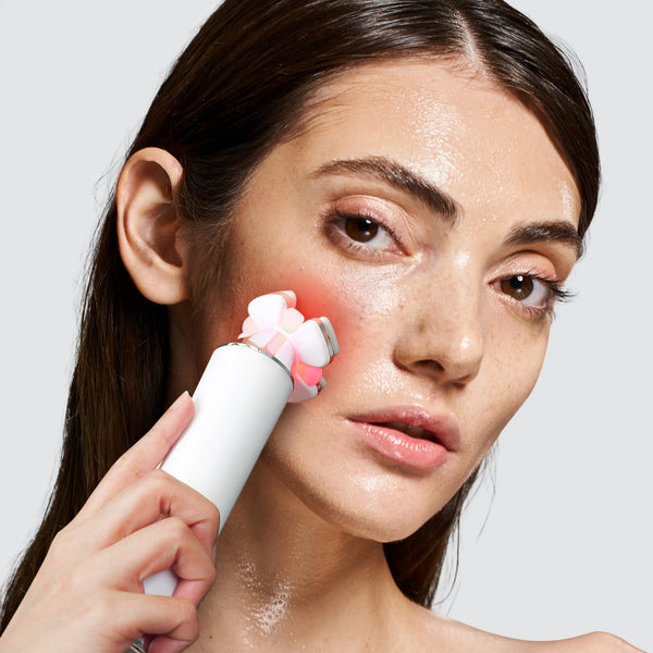 Halio RevitaWave skincare wand with glowing LED head pressed against a woman's cheek.
