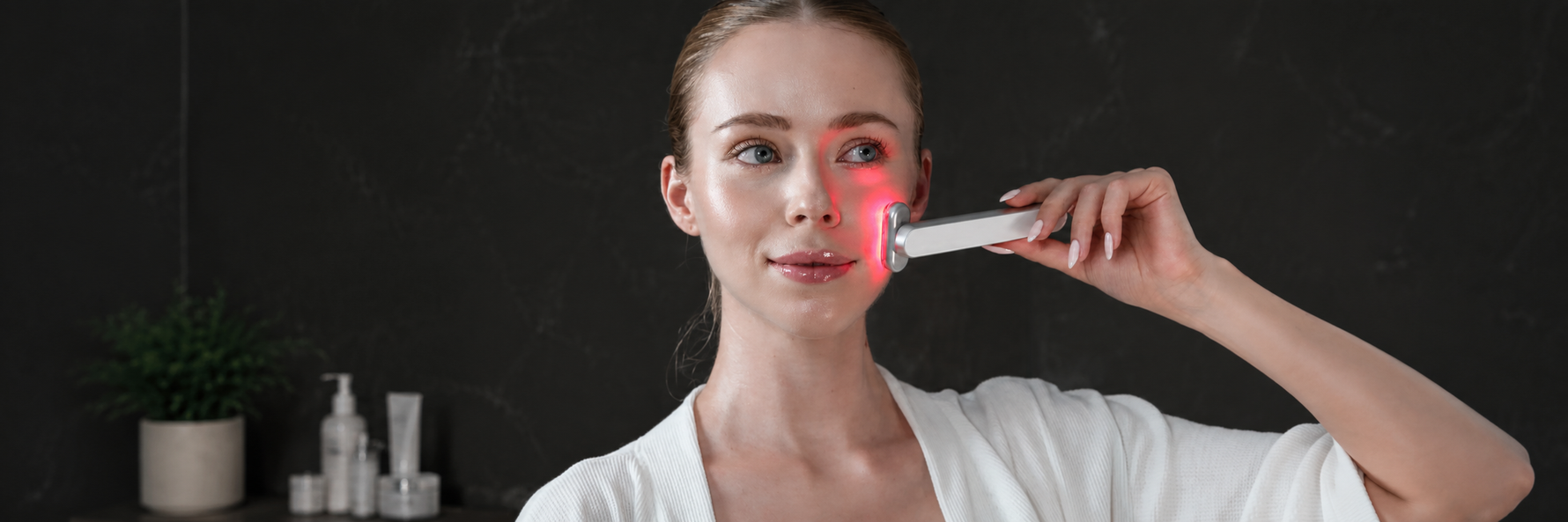 Person using a red light therapy wand on the jawline area during an evening skincare routine at the bathroom mirror