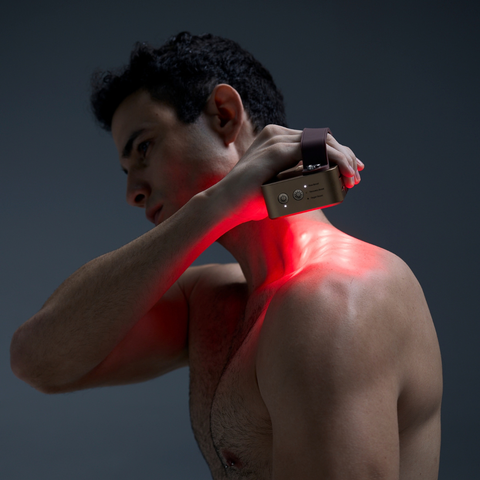 Man holding a Halio red light therapy device against his neck, casting a red glow across his shoulder and chest