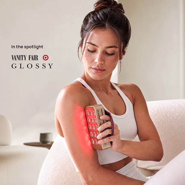 Woman holding the Halio RegenBoost red light panel against her upper arm, with red light glowing on her skin.