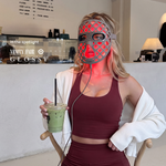 Woman wearing a glowing red Halio PureGlow LED face mask, burgundy outfit, and holding a matcha drink; “In the spotlight VANY FAIR GLOSSY” visible.